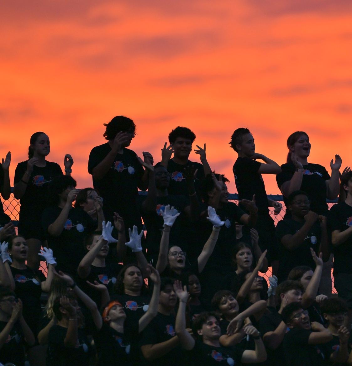 Warrior student section cheering against an orange sunset sky.