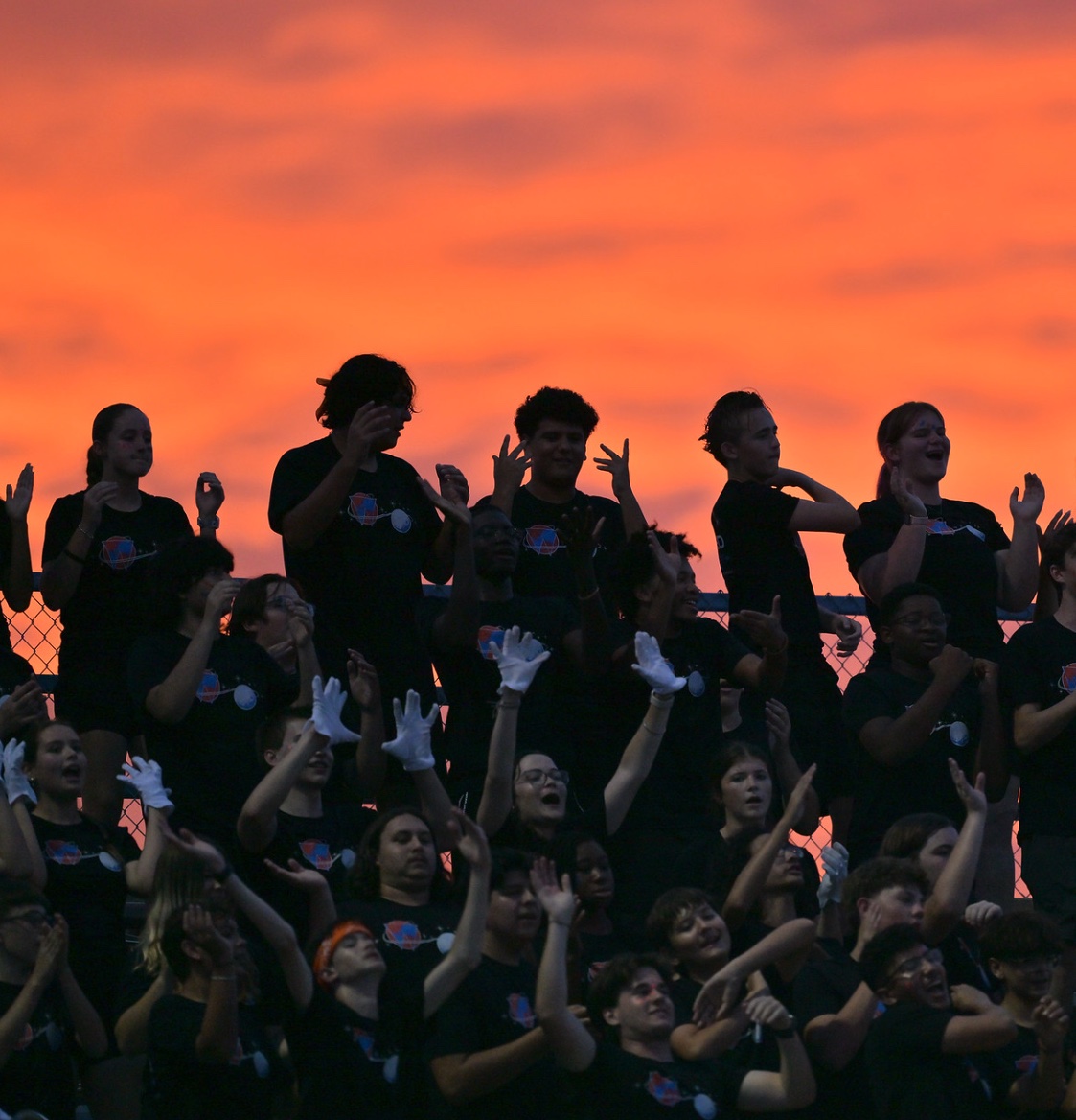 Warrior student section cheering against an orange sunset sky.